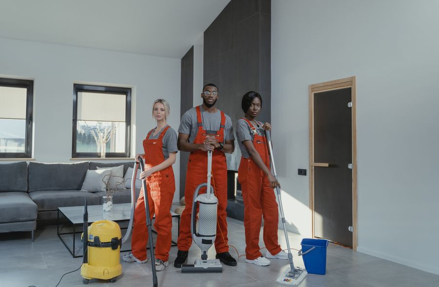 Three cleaners in matching work uniforms with a vacuum, mop, and cleaning supplies