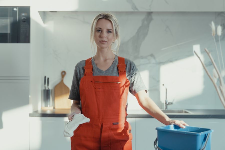 Cleaner in matching work uniform with a bucket and supplies