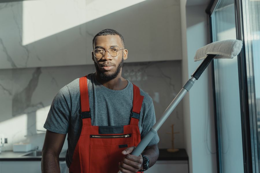 Uniformed cleaner holding a mop beside glass doors